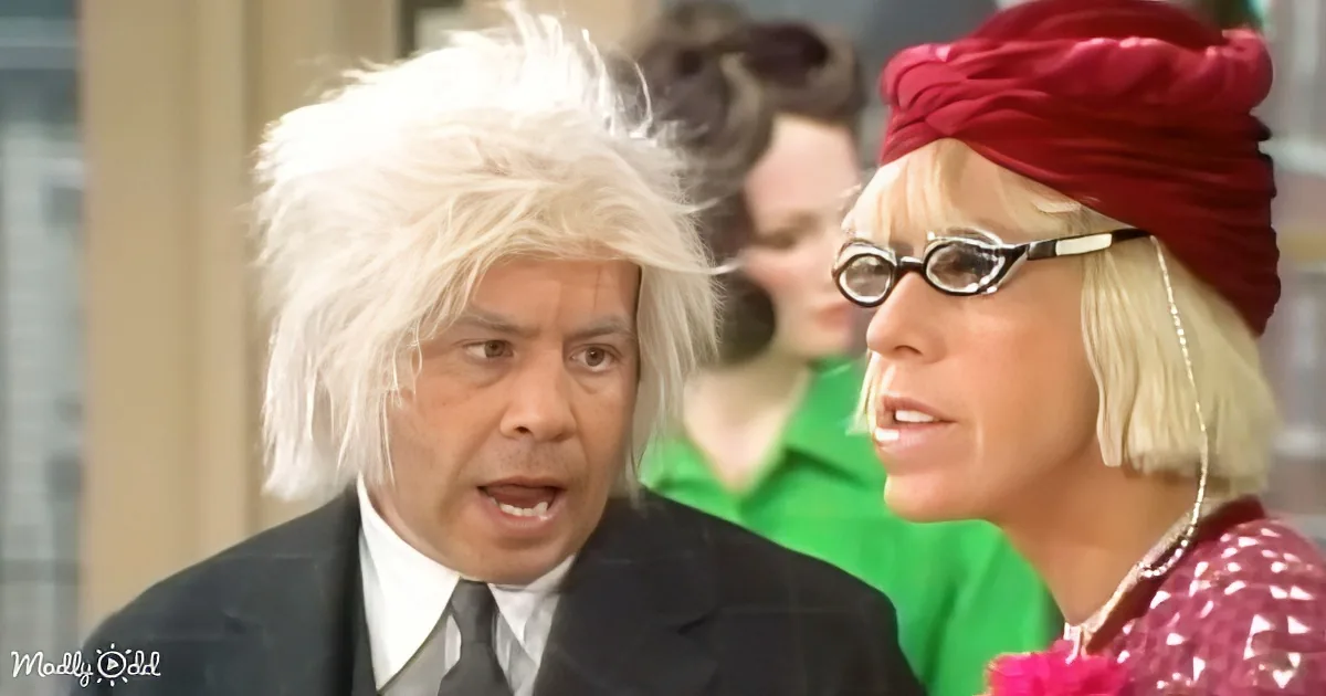 A man in a suit with a white wig and a woman in a red turban and glasses are in a scene.