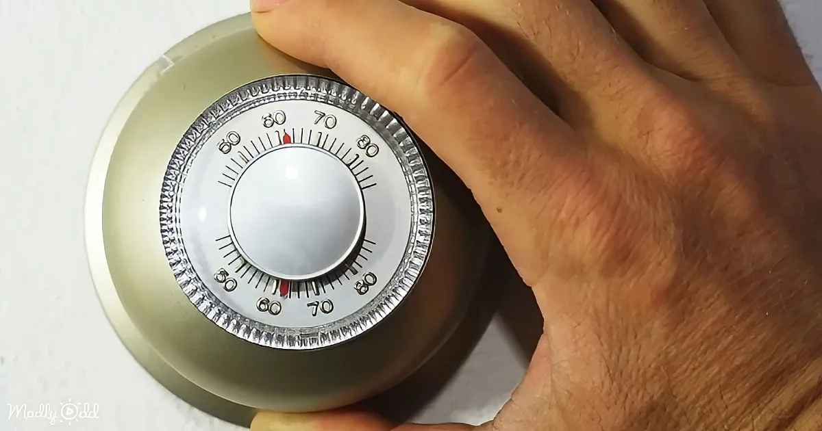 A hand adjusts a thermostat with a dial showing temperature settings.