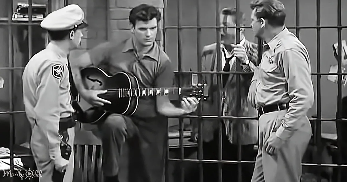 A man in uniform plays guitar while another in uniform and others watch in a jail setting.