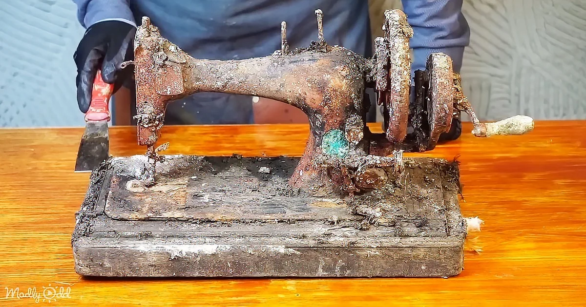 An old, rusted sewing machine sits on a wooden table, covered in dirt and debris.