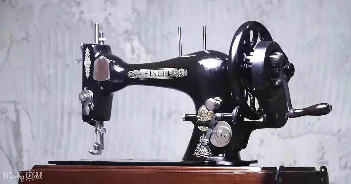 A vintage black Singer sewing machine with ornate details sits on a wooden surface against a textured wall.