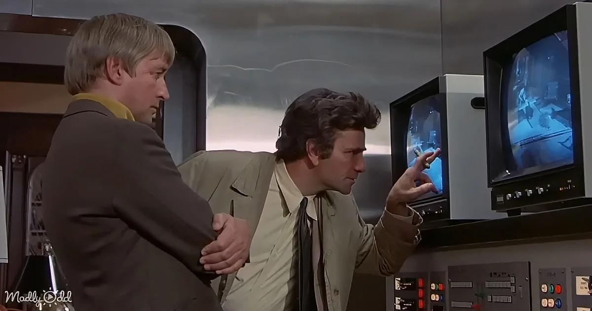 Two men in a control room, one pointing at a monitor, discussing something.