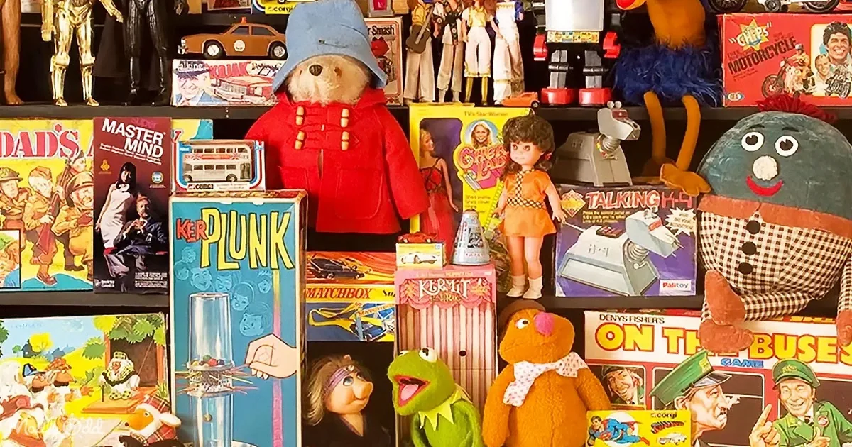 A Paddington Bear figure in a red coat and blue hat stands among vintage toys and board games.