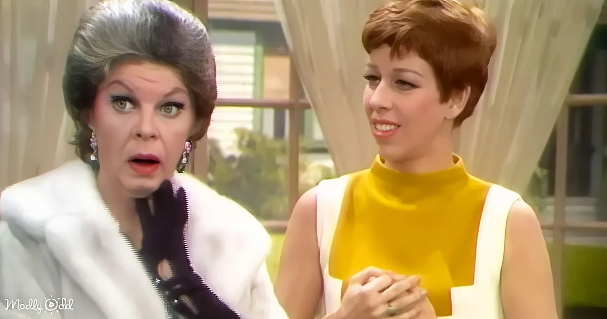 Two women, one in white, the other in yellow, appear to be in a conversation in a room with curtains.