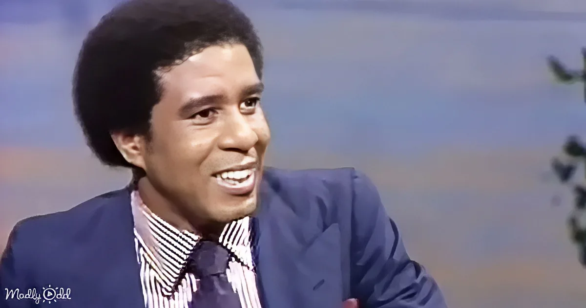 A man in a suit and striped shirt smiles widely, appearing joyful, against a blurred background.