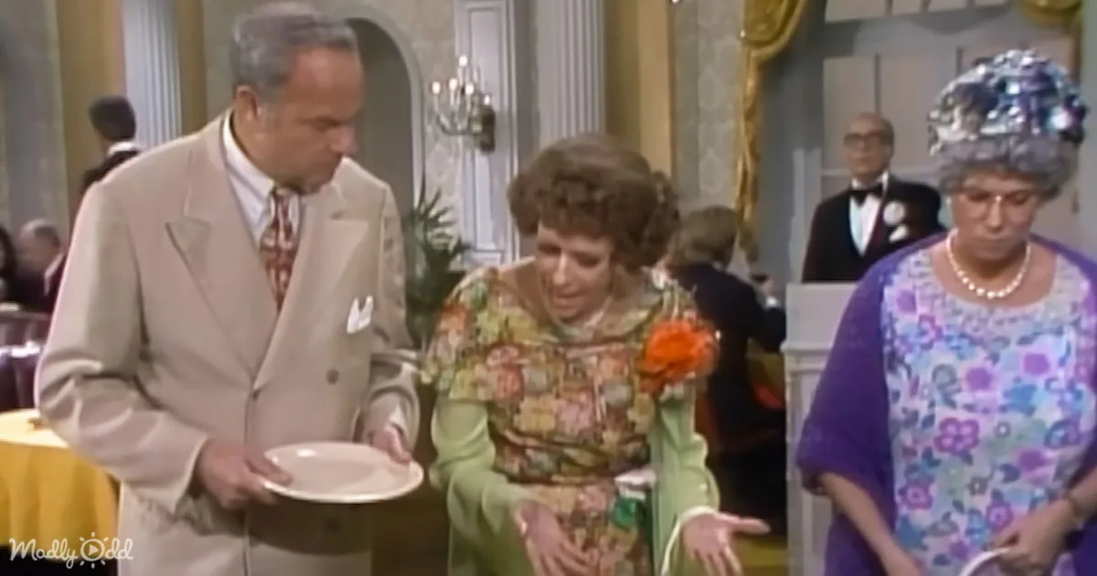 A man in a beige suit holds a plate, standing next to a woman in a floral dress, with another woman in a purple dress and...