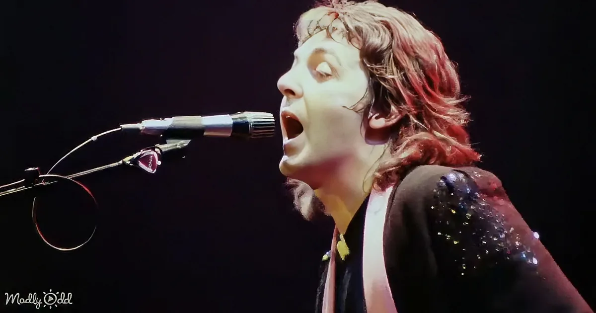 A person with long hair singing into a microphone, wearing a black shirt with glittery details.