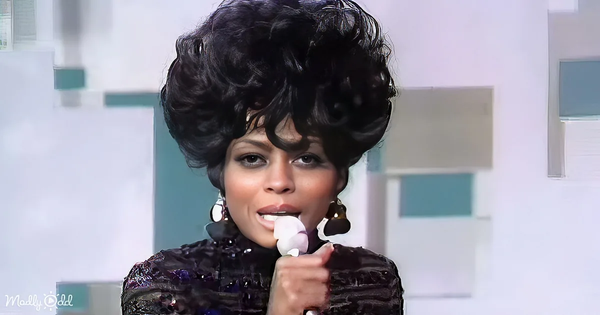A person with voluminous hair and a dark outfit holds a white object near their mouth.