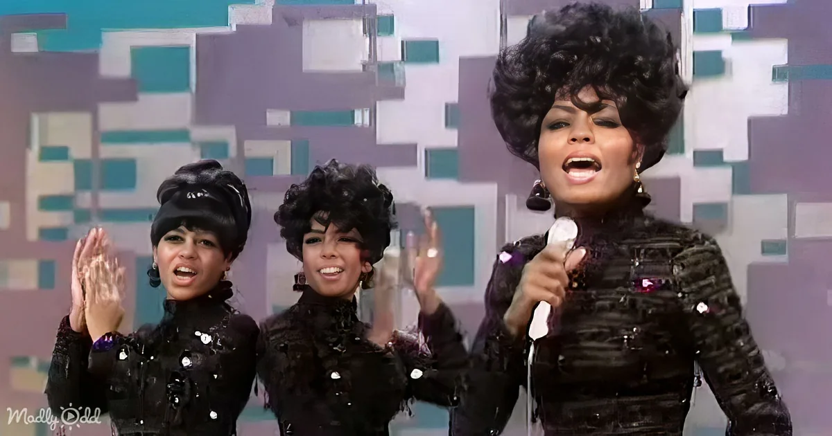 A woman in a black outfit with a microphone sings passionately, accompanied by two other women in similar attire.