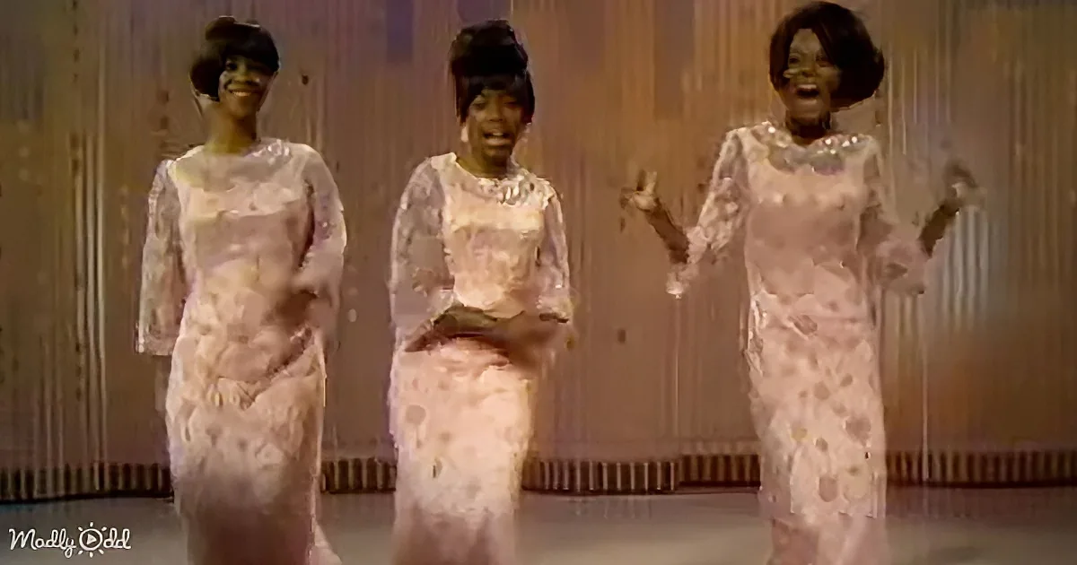 Three women in matching pink dresses perform a synchronized dance on stage.