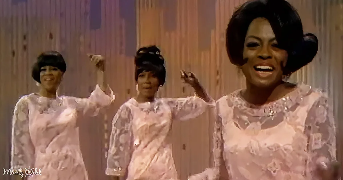 A woman in a pink lace dress smiles and raises her hand, joined by two others in matching outfits.