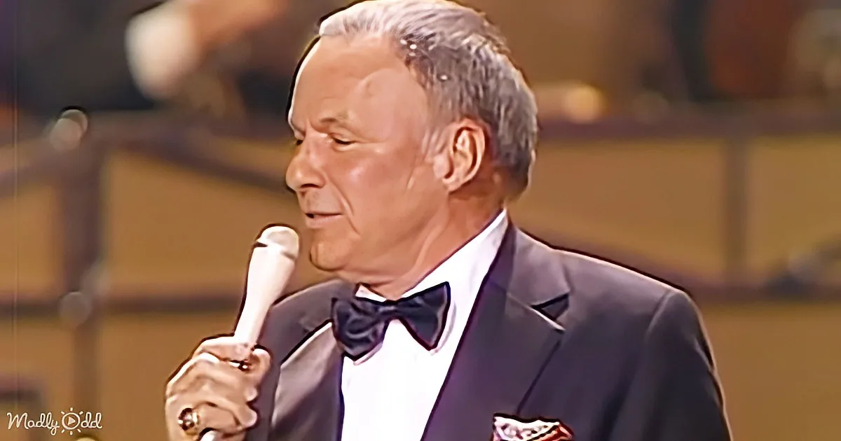 A man in a tuxedo holding a microphone, wearing a bow tie, and singing on stage.