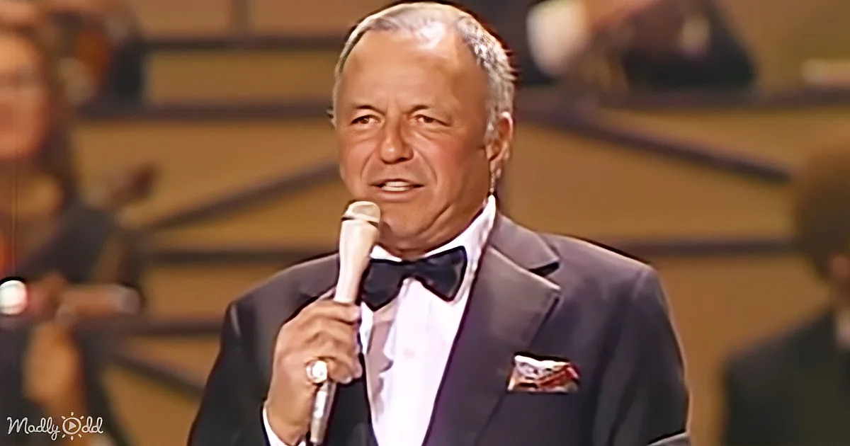 A man in a tuxedo holding a microphone, wearing a bow tie, and speaking on stage.