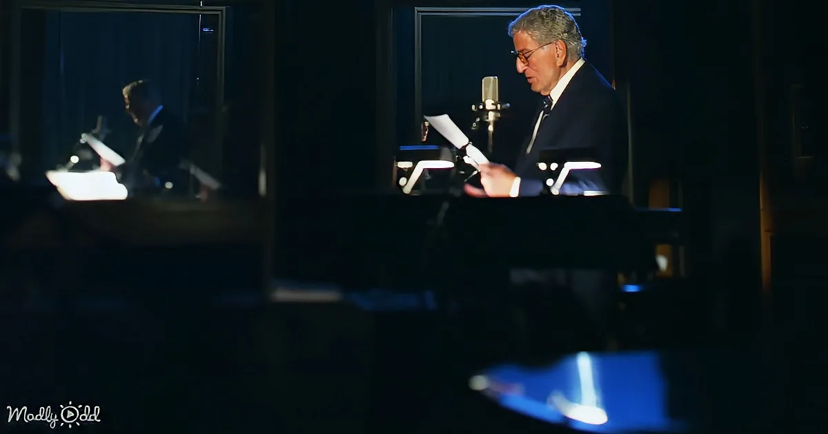 A man in a suit sits at a desk, reading from a sheet of paper in a dimly lit room.
