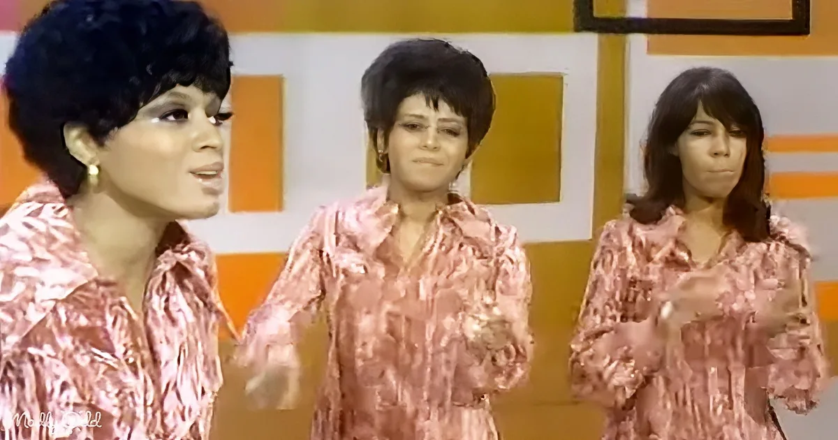 Three women in matching pink patterned shirts stand against a colorful geometric background.