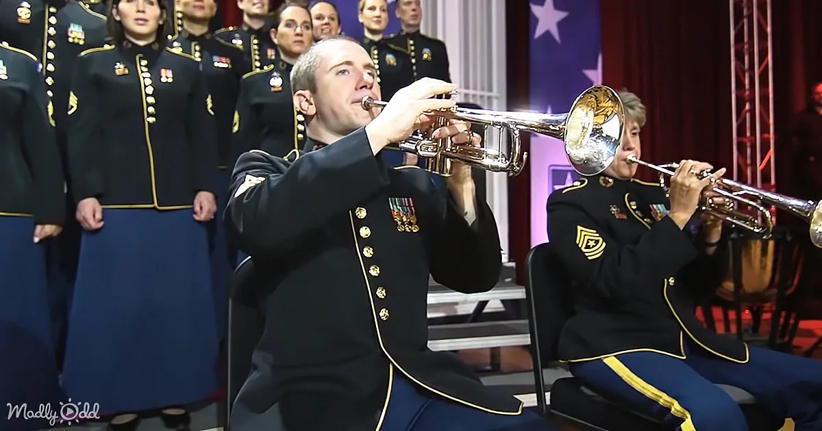 A man in military uniform plays trumpet in front of a choir and another musician.