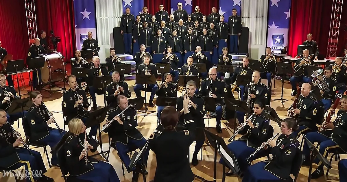 A military band in uniform plays instruments under a red curtain with American flag motifs.