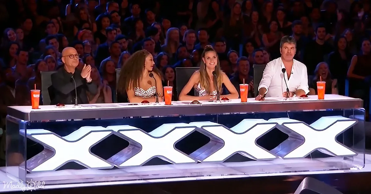 Judges at a talent show with "X" logo, audience in the background, drinks on the table.