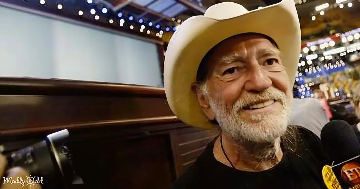 A man wearing a cowboy hat smiles while being interviewed in a brightly lit venue.