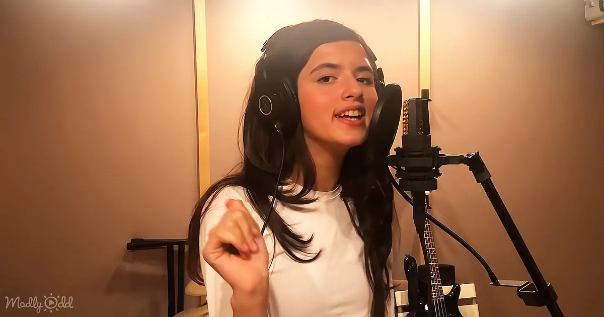A person wearing headphones sings into a microphone in a warmly lit room.