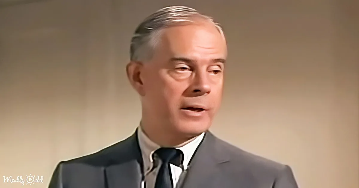 A man in a suit and tie is speaking, with a neutral background.