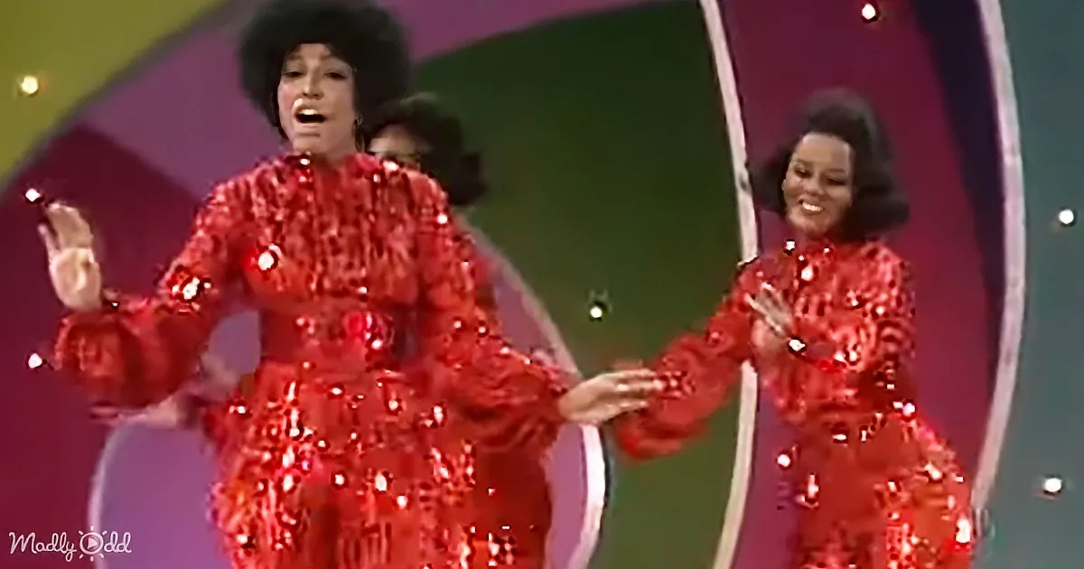 Two women in red sequined outfits perform on stage, one holding a microphone.