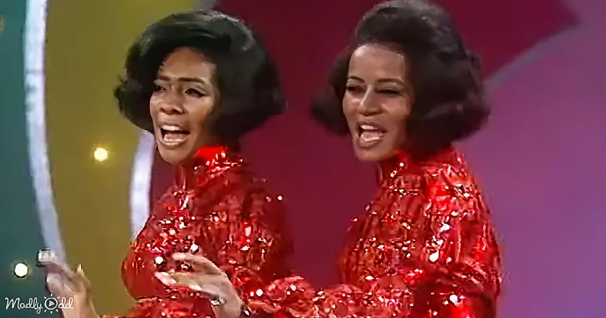 Two women in red sequined outfits perform on stage with vibrant lighting and colorful background.