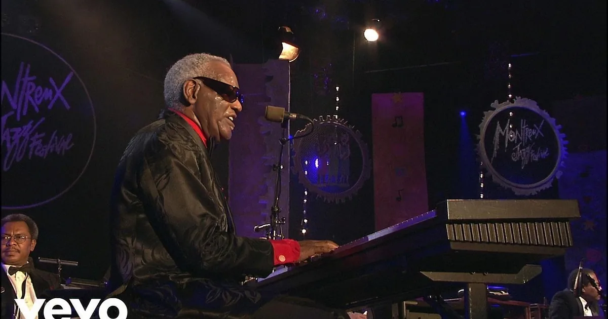 A man in sunglasses plays piano at Montreux Jazz Festival, illuminated stage with colorful lights.
