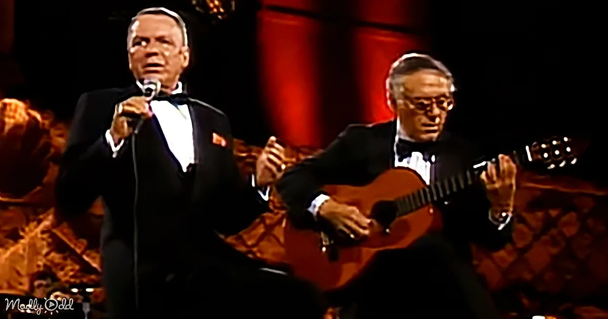 Frank Sinatra in tuxedo sings into microphone, accompanied by man playing guitar in formal attire.
