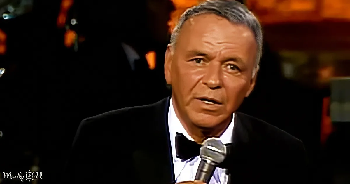 A man in a tuxedo speaks into a microphone, likely performing or hosting an event.