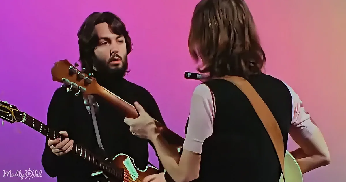 A man with long hair and beard plays guitar, another person sings into a microphone.