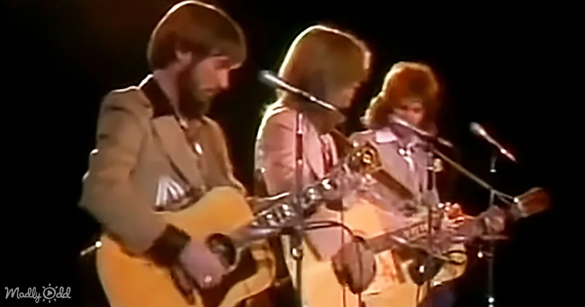A man in a suit plays guitar on stage with two other musicians.