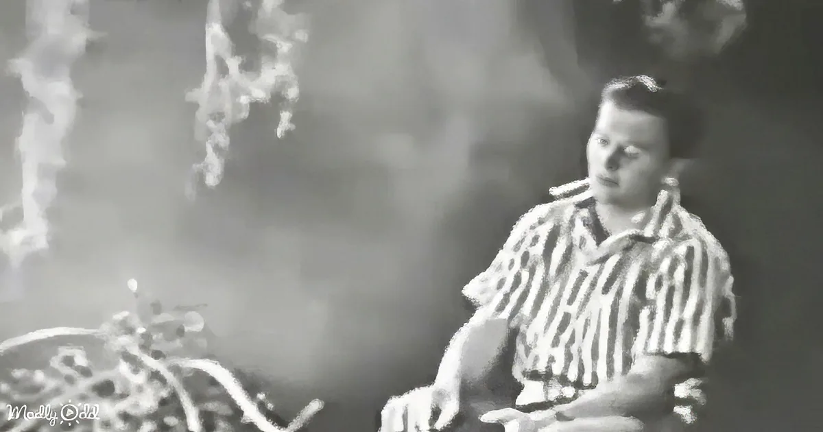A man in a striped shirt is playing drums with a microphone in front of him, surrounded by smoke.