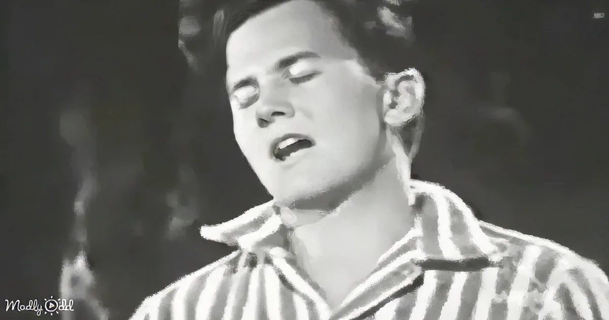 A person in a striped shirt sings passionately, mouth open, eyes closed, in a black-and-white setting.