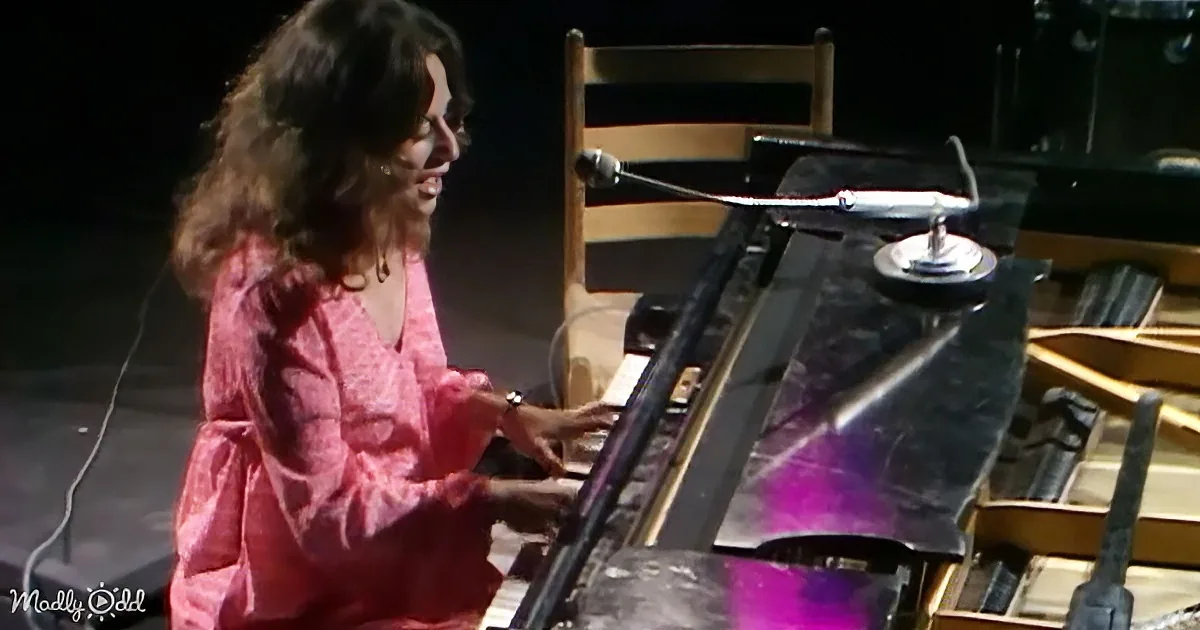 A woman in a pink dress plays a piano on stage with a microphone.