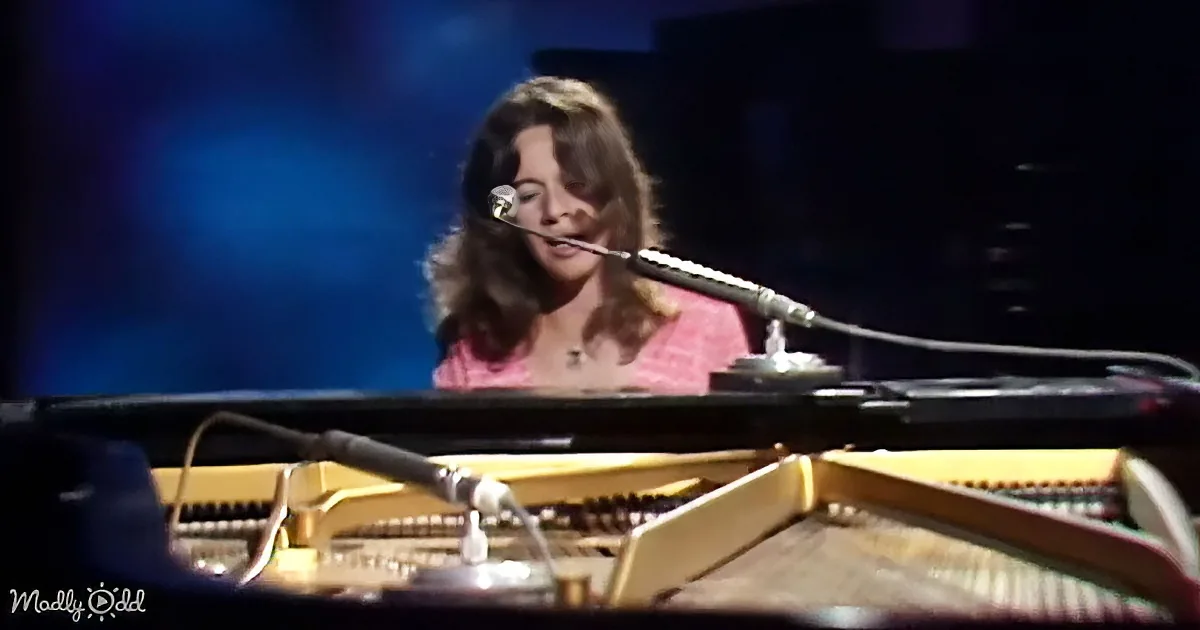 A woman sings into a microphone while playing a grand piano on stage.