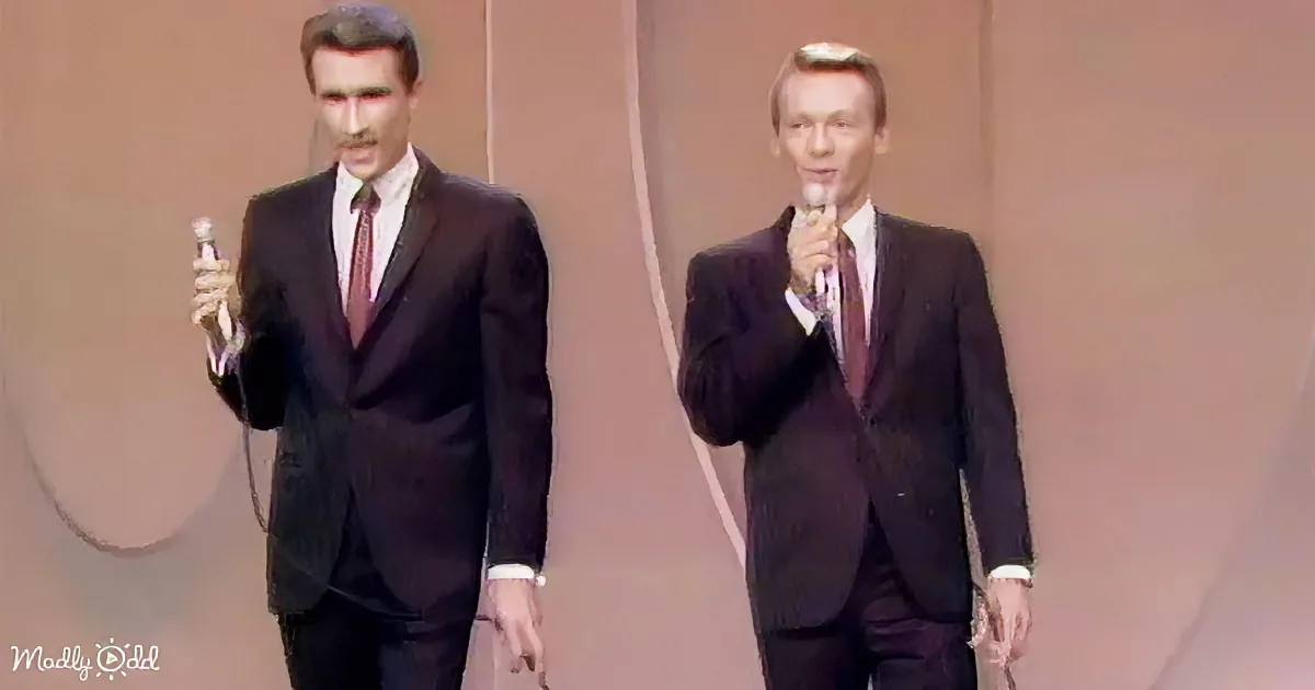 Two men in suits holding microphones, standing side by side on a stage.