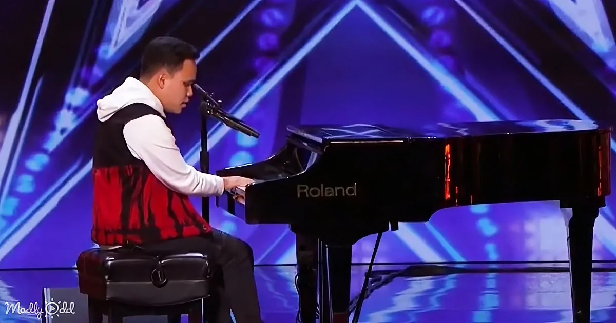 A man in a red vest plays a black Roland piano on a stage with blue lighting.
