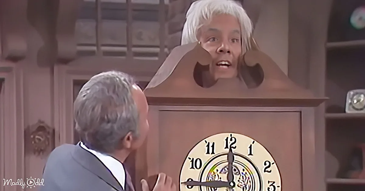 A person in a suit interacts with a large clock, where a person's head is inside the clock's face.