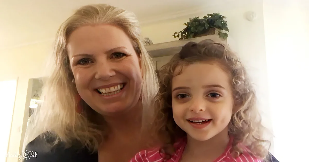 A smiling woman with blonde hair and a young girl with curly hair are posing together indoors.