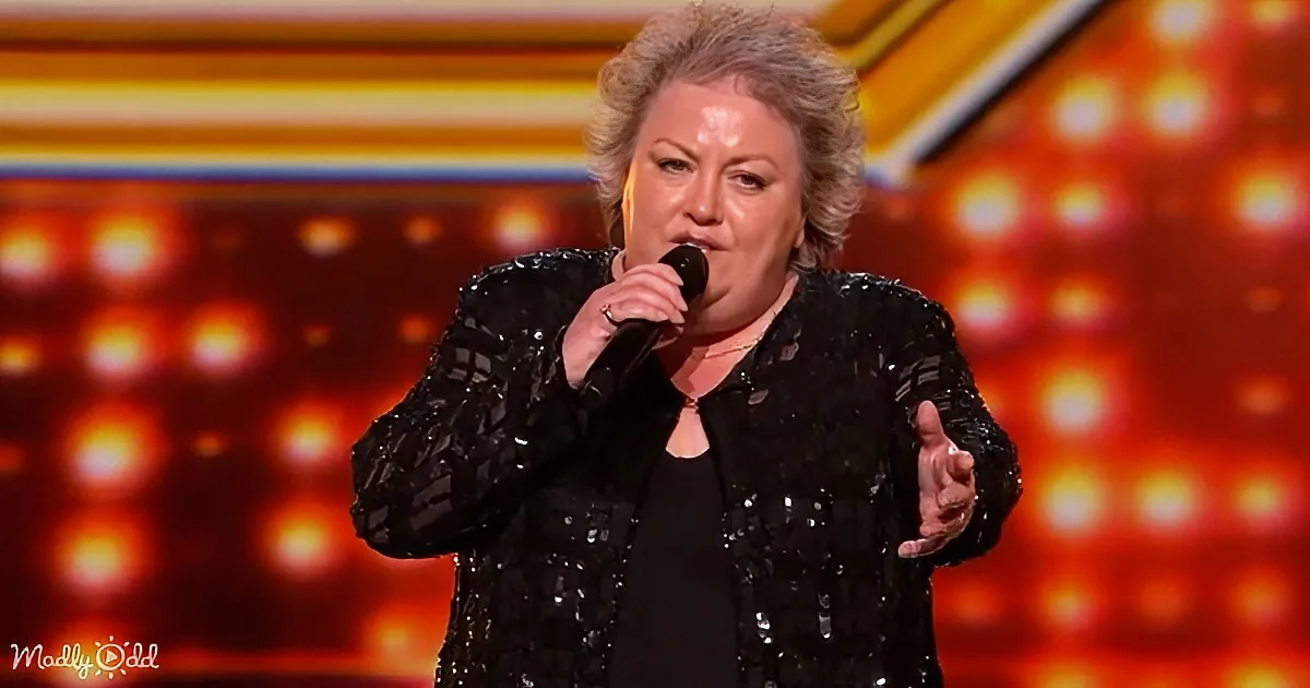 A woman in a black sequined jacket sings into a microphone on a stage with bright lights.
