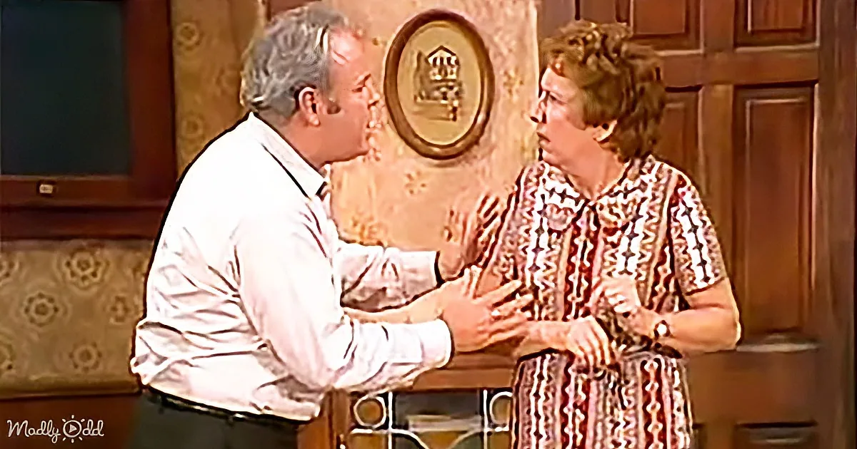 A man in a white shirt leans towards a woman in a patterned shirt, both appearing engaged in conversation.