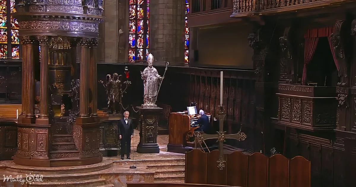 A man in a suit stands at a podium in a grand church with stained glass and ornate architecture.