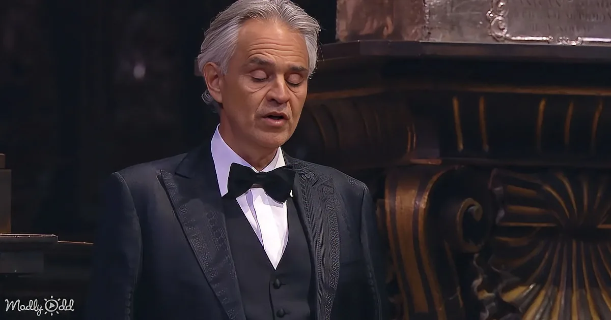 A man in a tuxedo with a bow tie stands in front of ornate furniture, appearing to sing or speak.