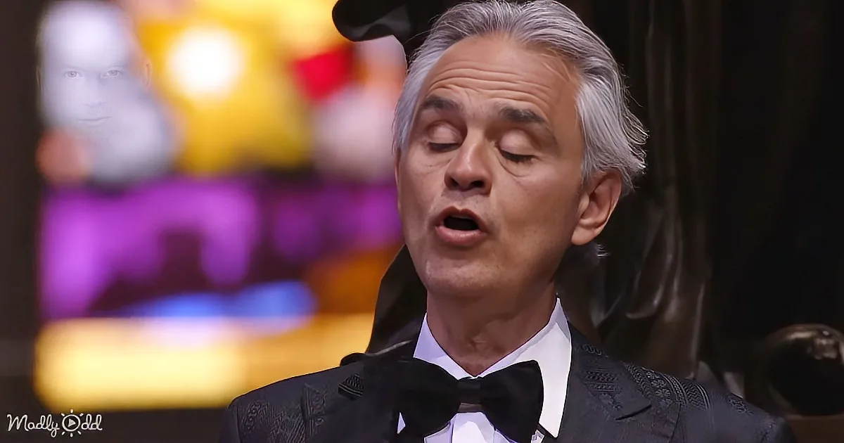 A man in a tuxedo sings with eyes closed, wearing a bow tie, in a dimly lit setting.