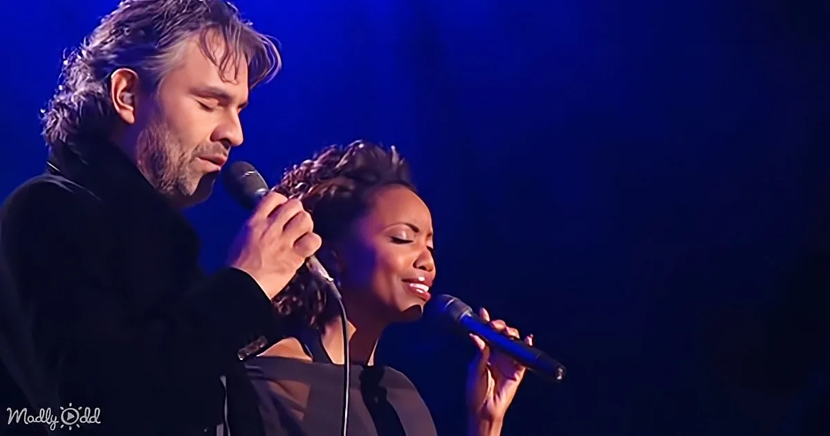 A man and woman sing into microphones on stage under blue lighting.
