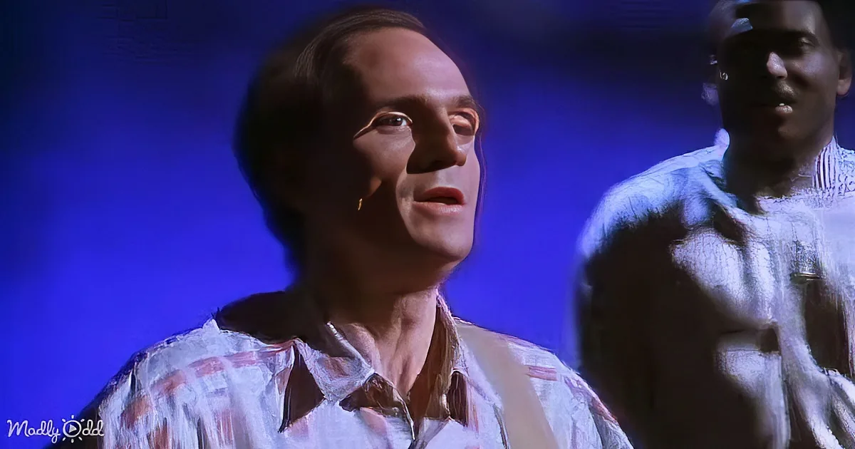 A man in a patterned shirt looks upward, with another person partially visible in the background.