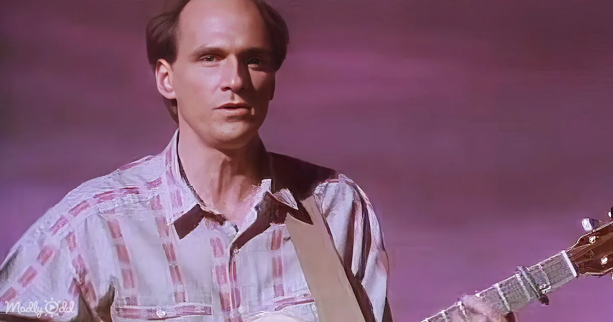 A man in a plaid shirt holds a guitar, set against a purple background.