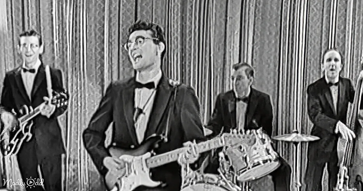 A man in a suit plays guitar while a band performs in a vintage setting.
