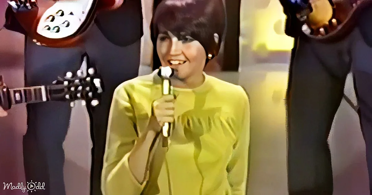 A woman in a yellow dress holds a microphone, smiling, with musicians in the background.